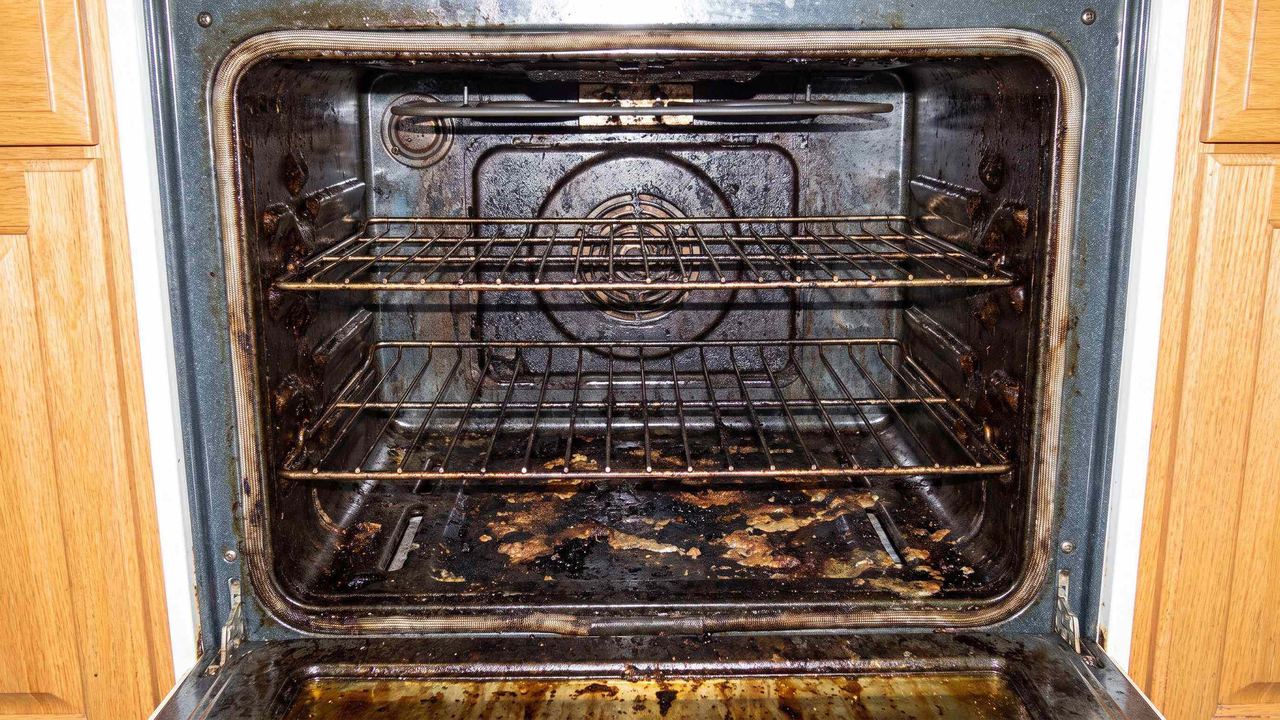 A heavily soiled oven interior, baked-on grease across the base and racks